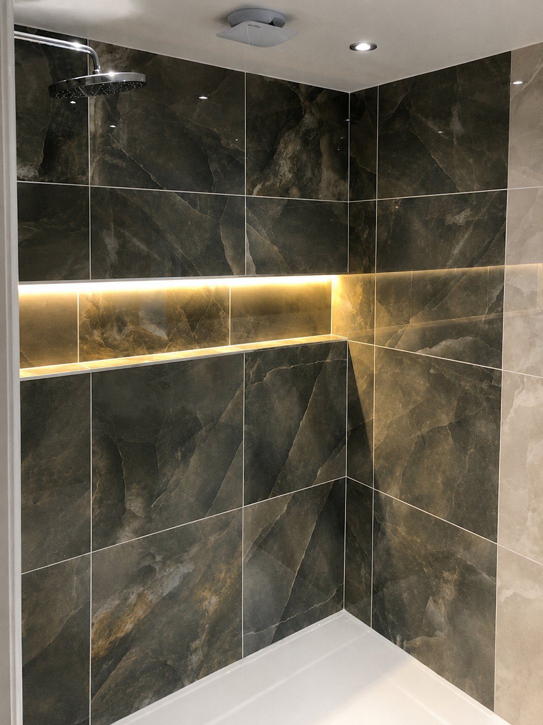 Finished walk-in shower by Andrade Renovations with dark marble tiling, brass detail and a backlit LED niche