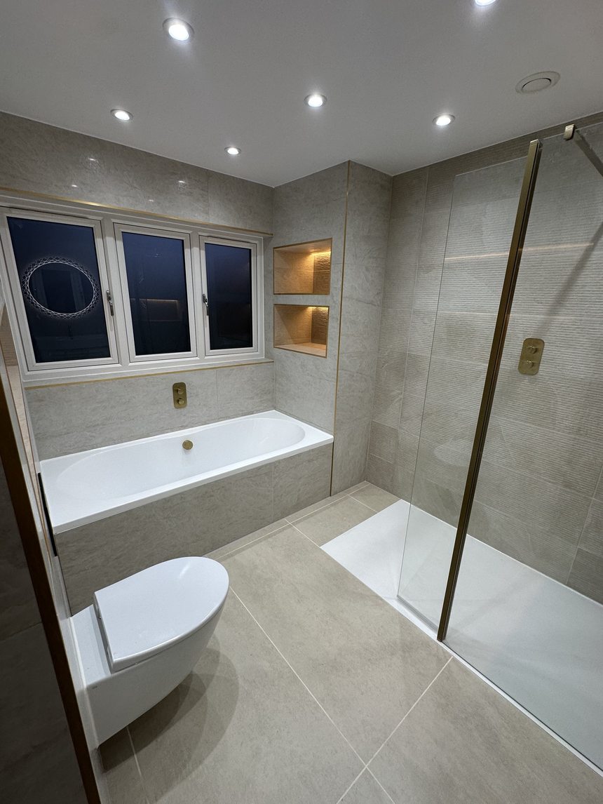 Finished bathroom by Andrade Renovations with grey marble tiling, brushed-gold fittings and lit niches